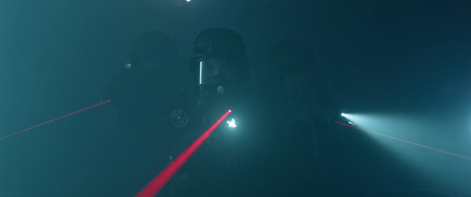 Grupo de agentes con cascos y equipo táctico en medio de una niebla azulada, con haces de láser rojos.