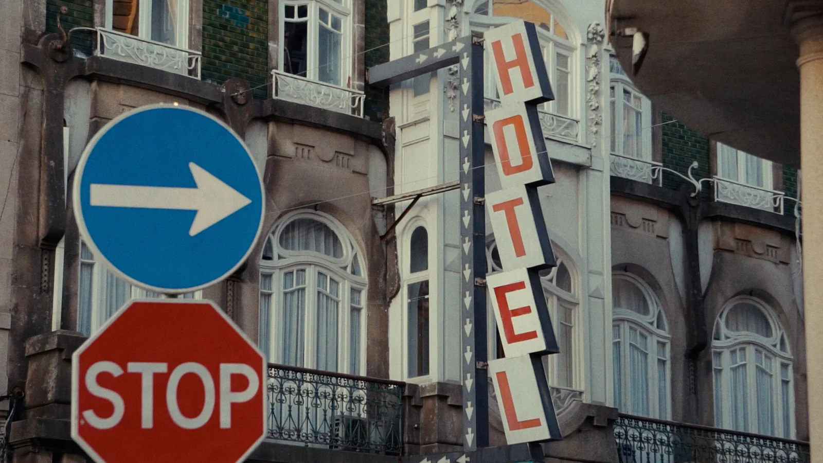 Fachada antigua con un rótulo vertical «HOTEL», una señal azul de dirección y otra roja de «STOP».