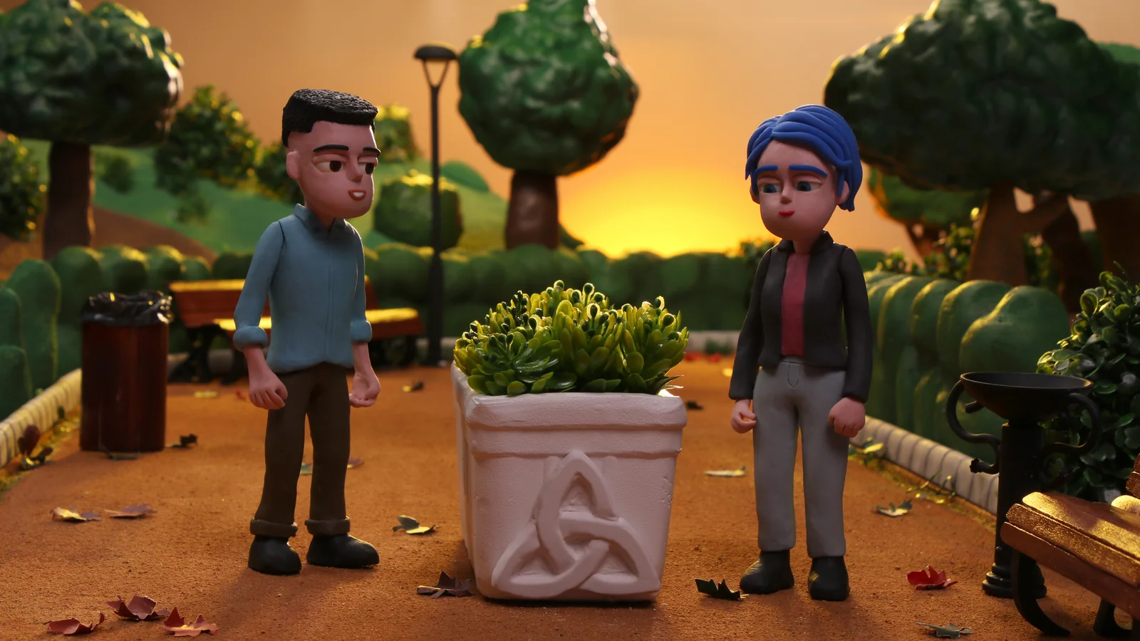 Animación en plastilina de dos personajes de pie en un parque al atardecer, entre árboles y una maceta.