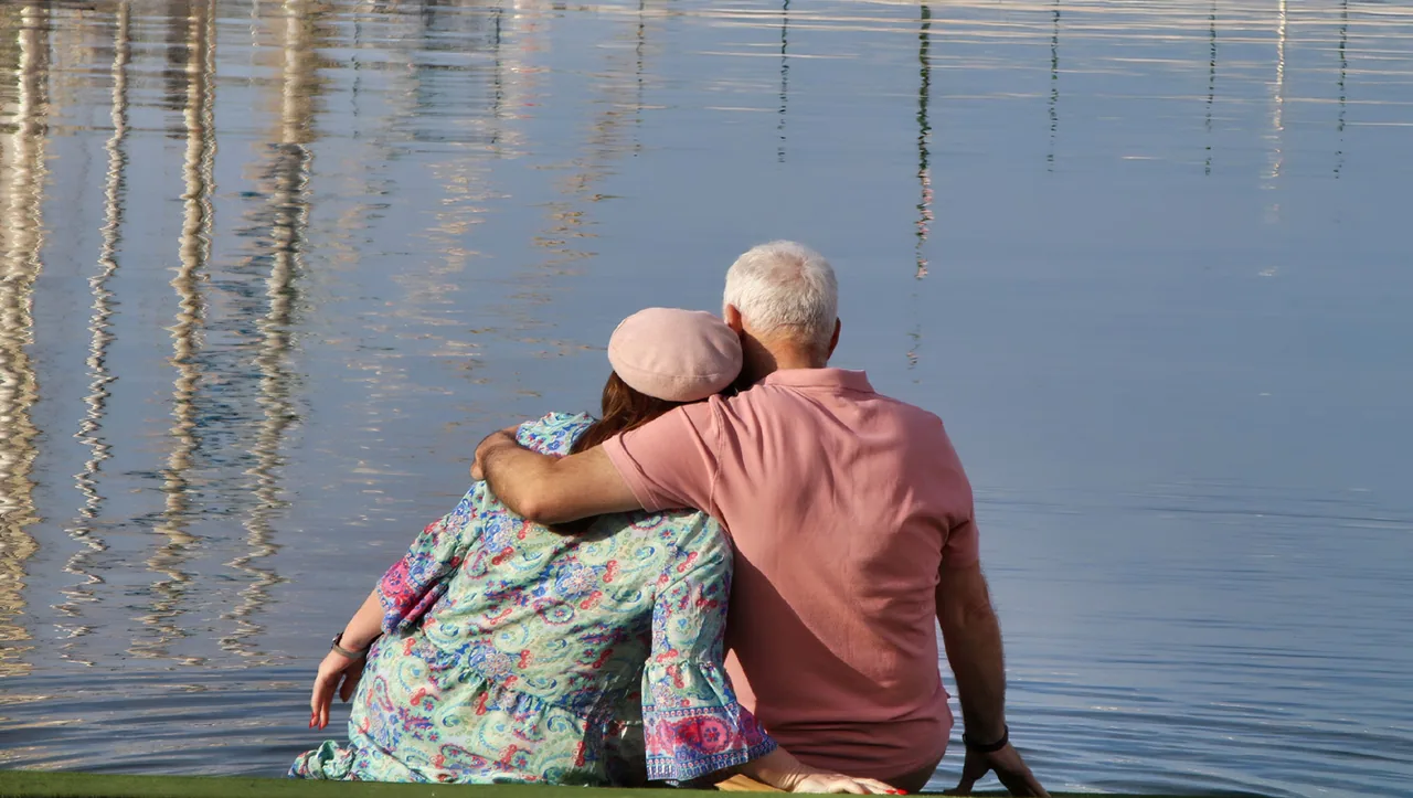 Fotograma de «Dejadme vivir»: una pareja mayor, de espaldas y abrazada, sentada frente al agua.