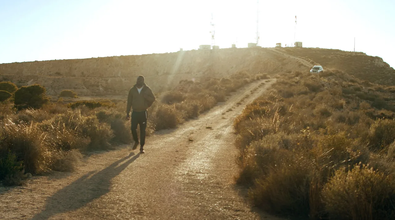Fotograma de «Un día cualquiera»: una persona camina de espaldas por un sendero de tierra hacia una loma, al atardecer.