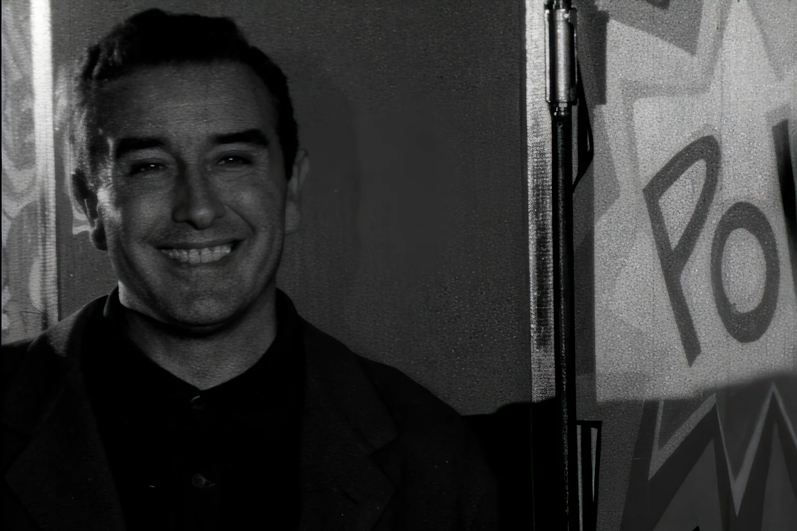 Fotograma de «Forqué. El oficio de hacer cine»: imagen en blanco y negro de un hombre joven que sonríe junto a un micrófono.