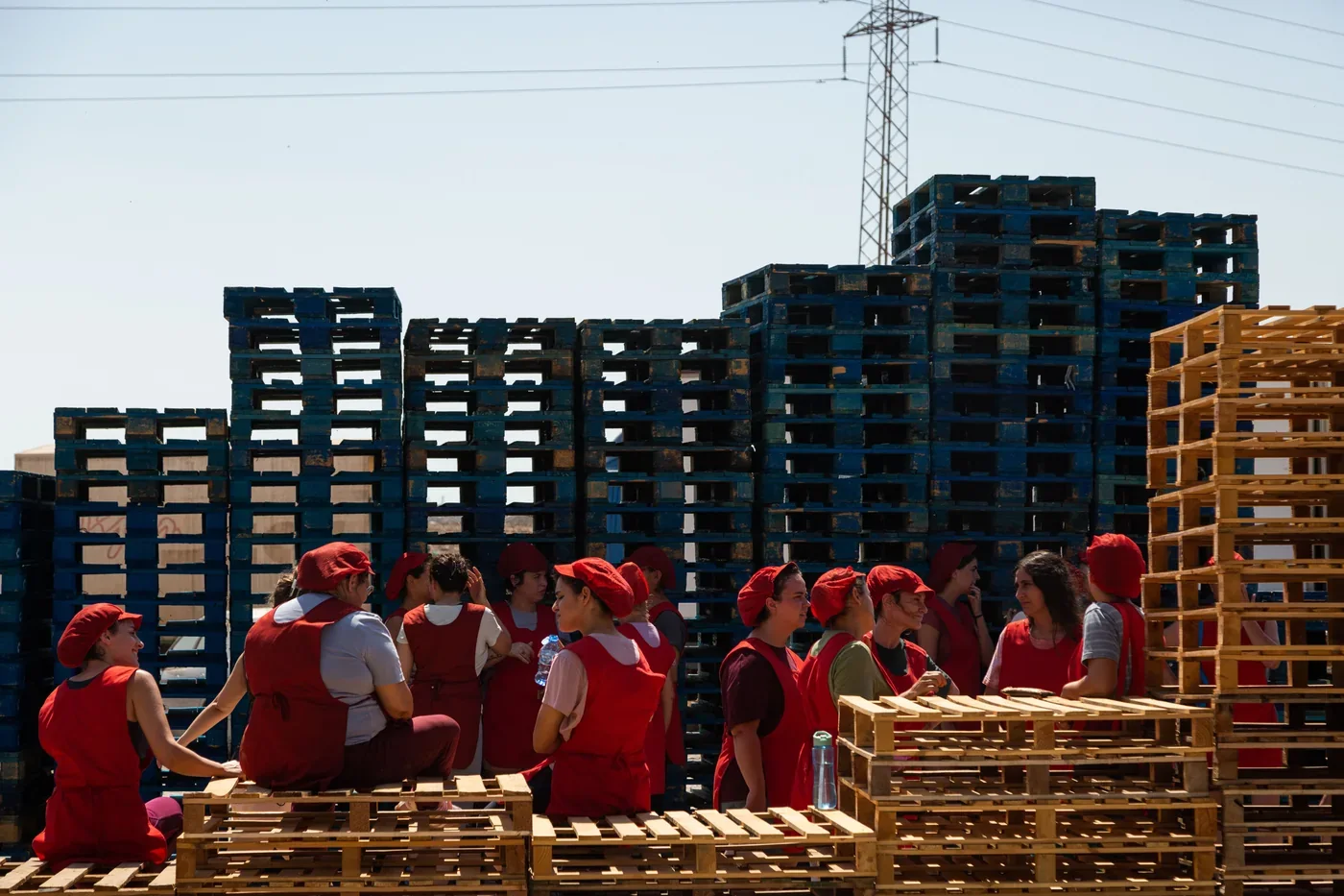 Fotograma de «Iván & Hadoum»: trabajadoras con uniforme rojo descansan sentadas sobre palés apilados.