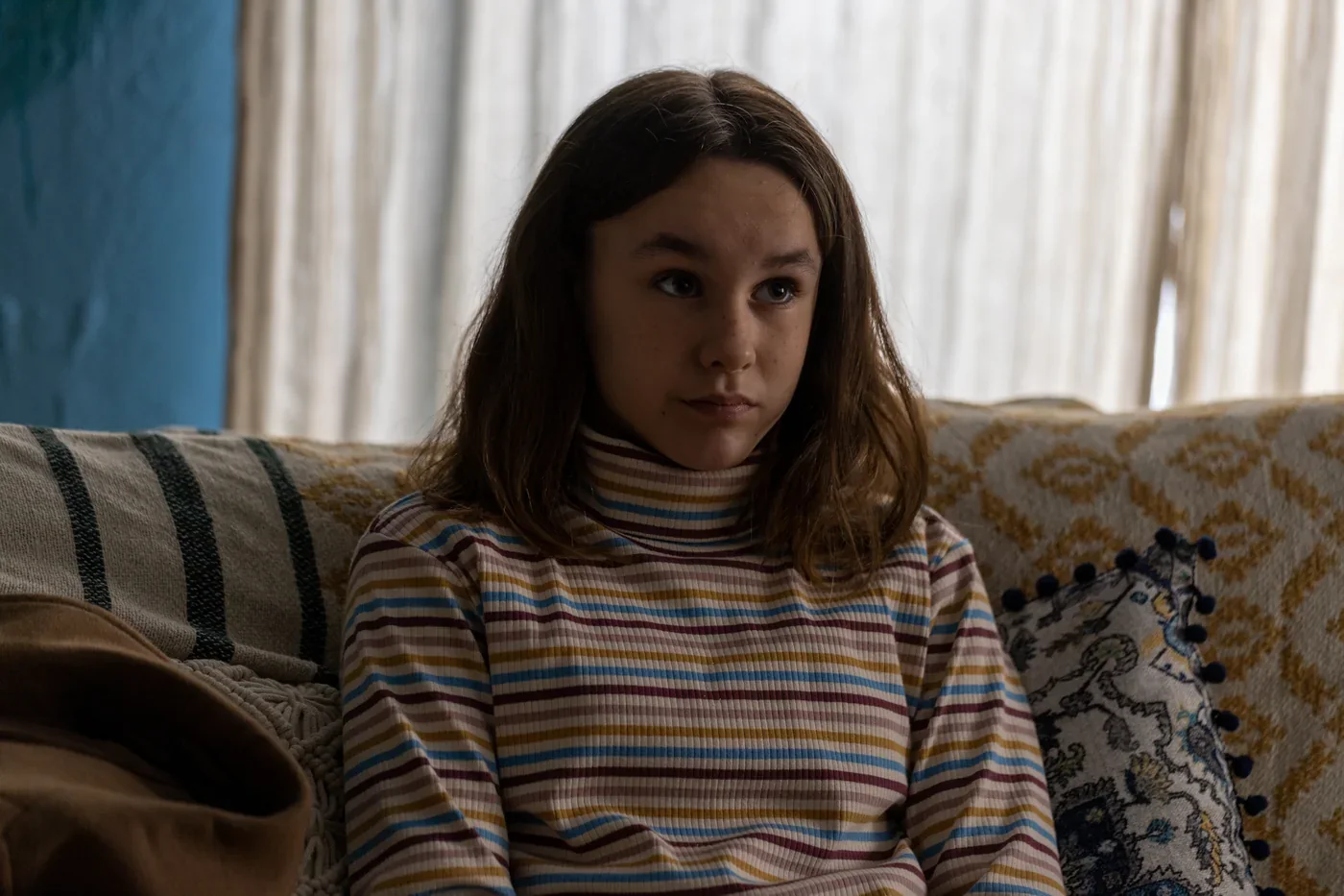 Fotograma de «La ventana abierta»: una adolescente con jersey de rayas, seria, sentada en un sofá.