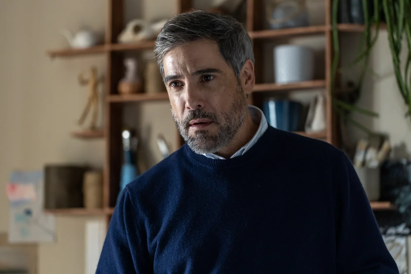 Fotograma de «La ventana abierta»: un hombre con jersey azul marino, preocupado, en una habitación con estanterías.